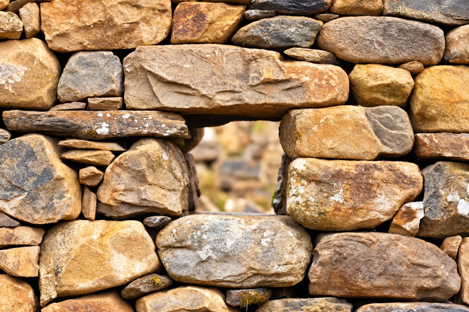 Natursteinmauer mit einer kleinen Öffnung, dahinter verschwommen Natur